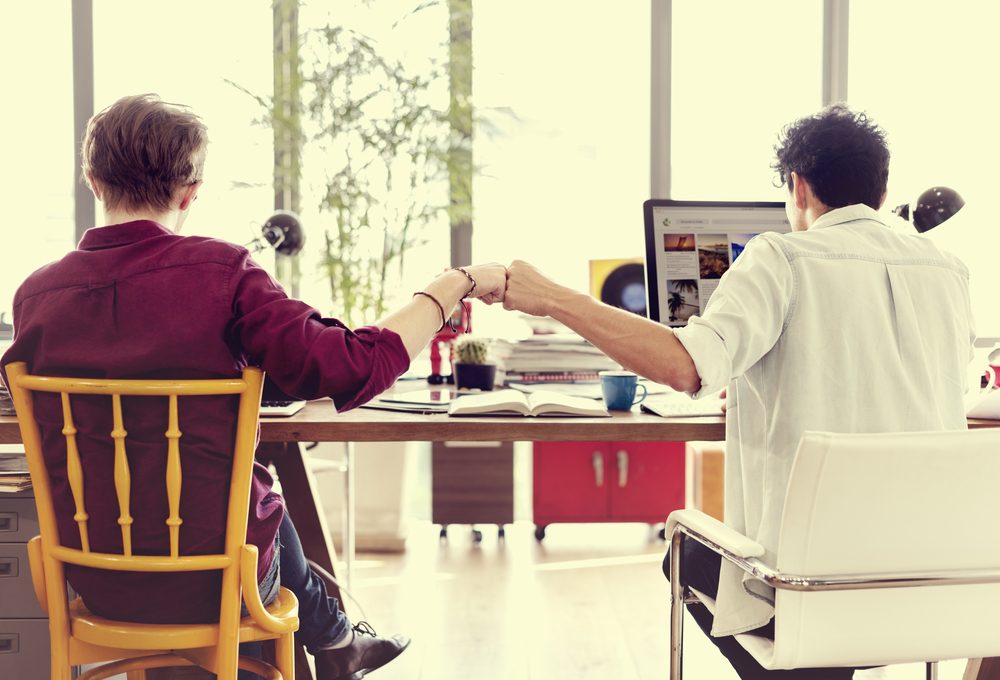 Two colleagues bumping fists across a desk